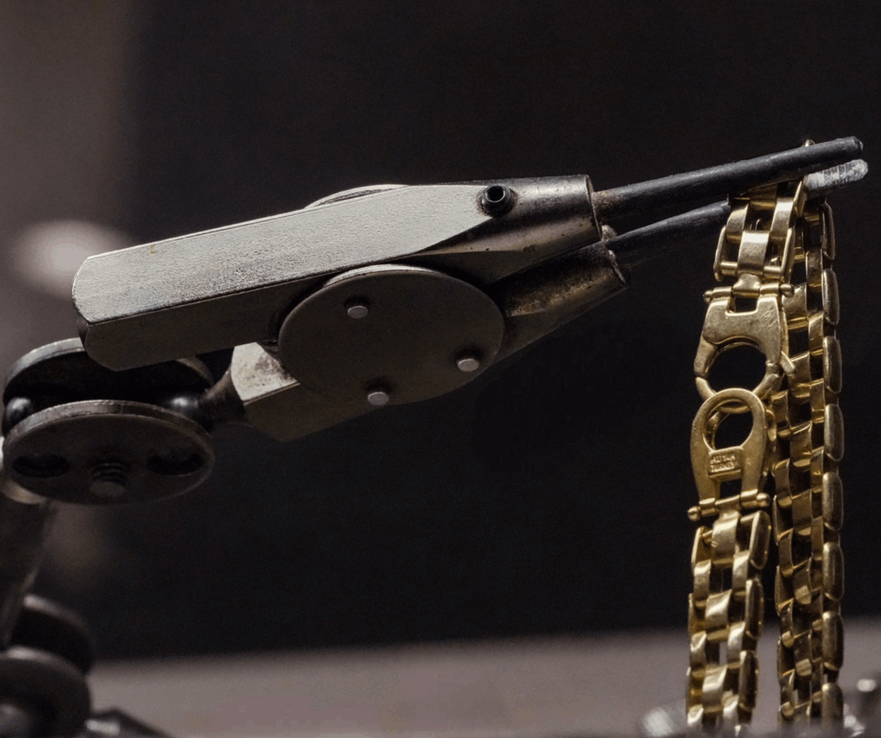 A gold link bracelet held by a jeweler's metal clamp