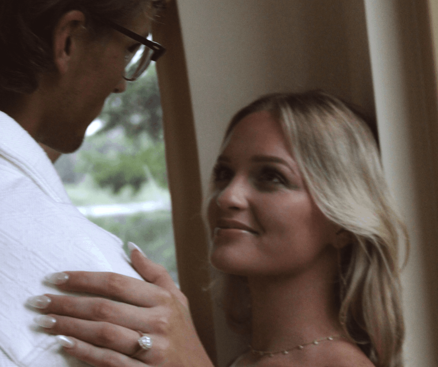 Close-up of an engaged couple smiling at each other, featuring a prominent diamond ring