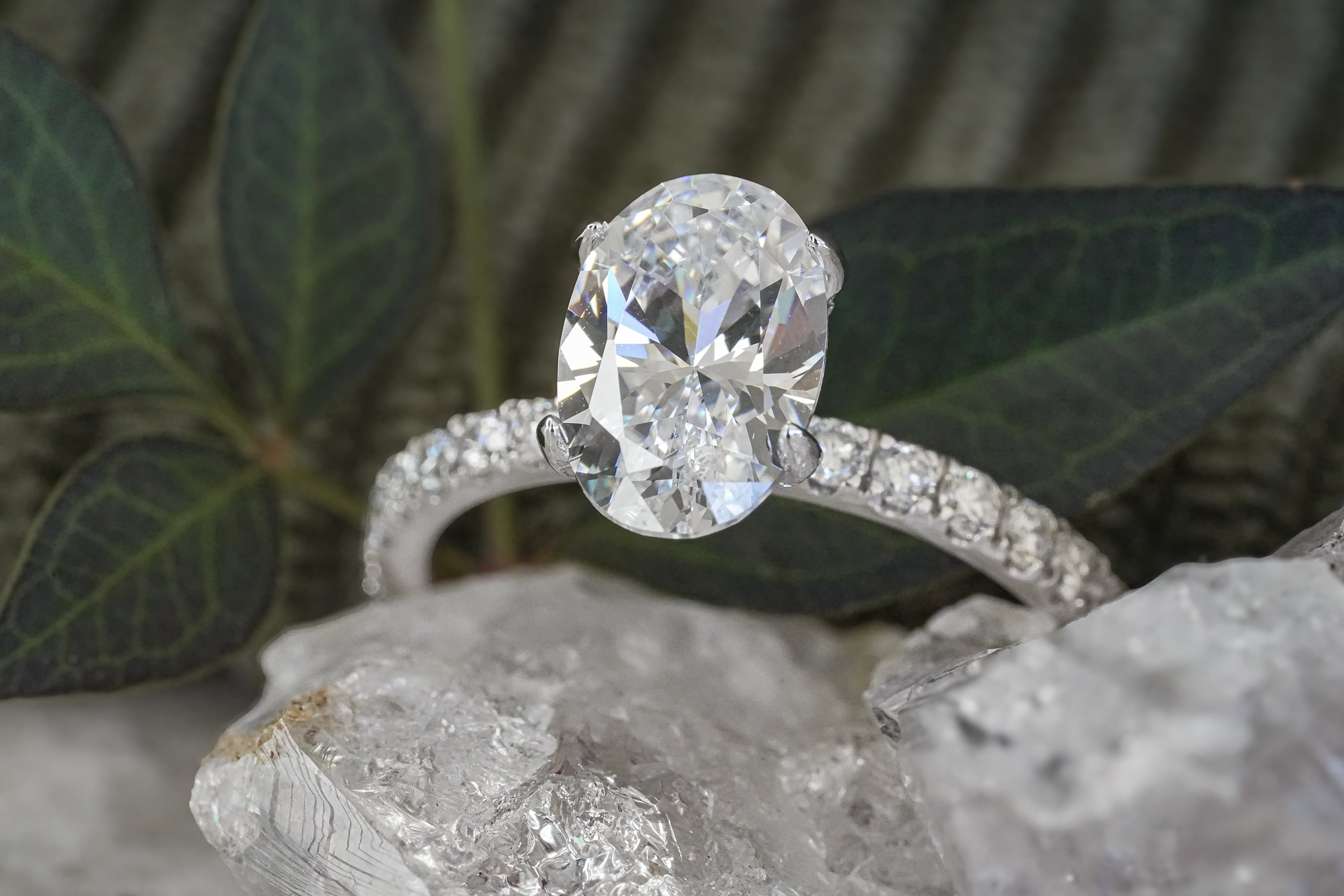 Silver or white gold engagement ring featuring a large oval-cut diamond solitaire on a pavé-set diamond band, resting on white crystal stones