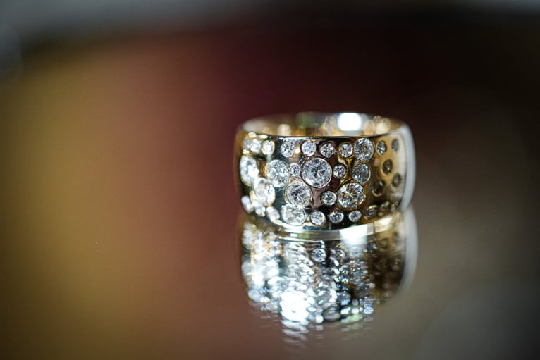 Wide gold and silver domed ring featuring a scattered cluster of various-sized round diamonds in a starry flush setting, reflecting on a dark surface